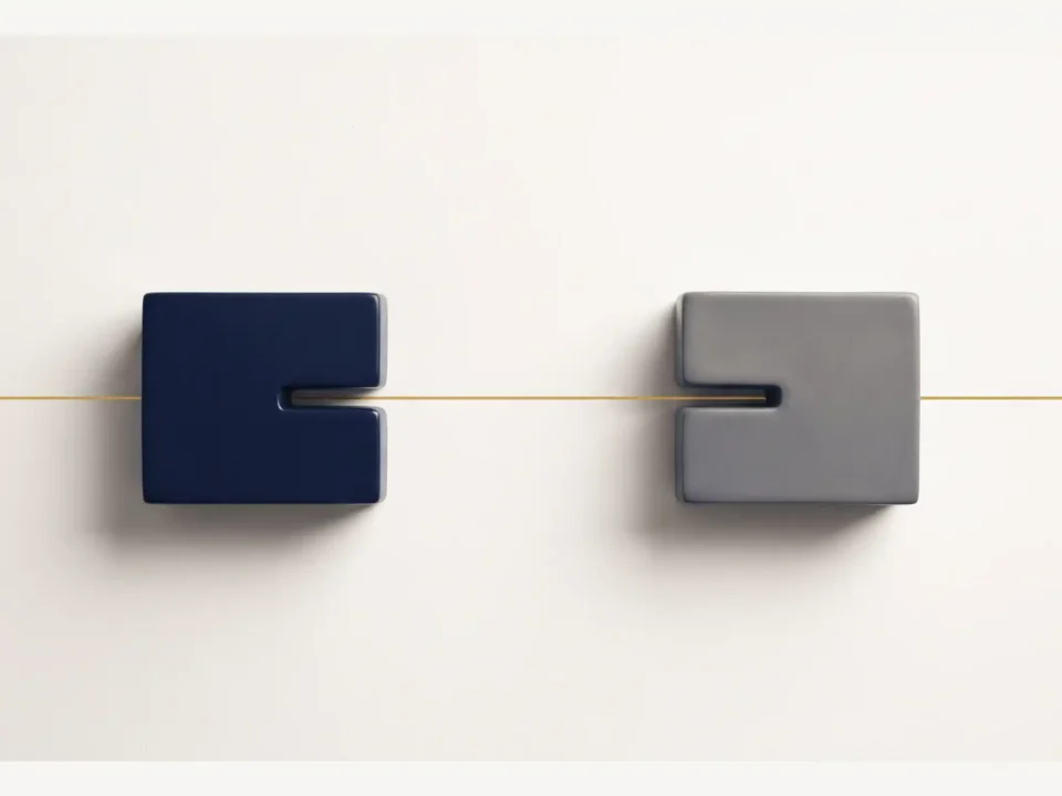 Due blocchi geometrici distinti, uno blu scuro e uno grigio, posizionati su uno sfondo chiaro e attraversati da una sottile linea metallica dorata.