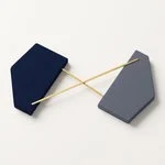 Composizione zenitale su superficie bianca calda con due blocchi geometrici ceramici distinti, uno blu marino e uno grigio, sormontati da una sottile linea metallica dorata orizzontale.