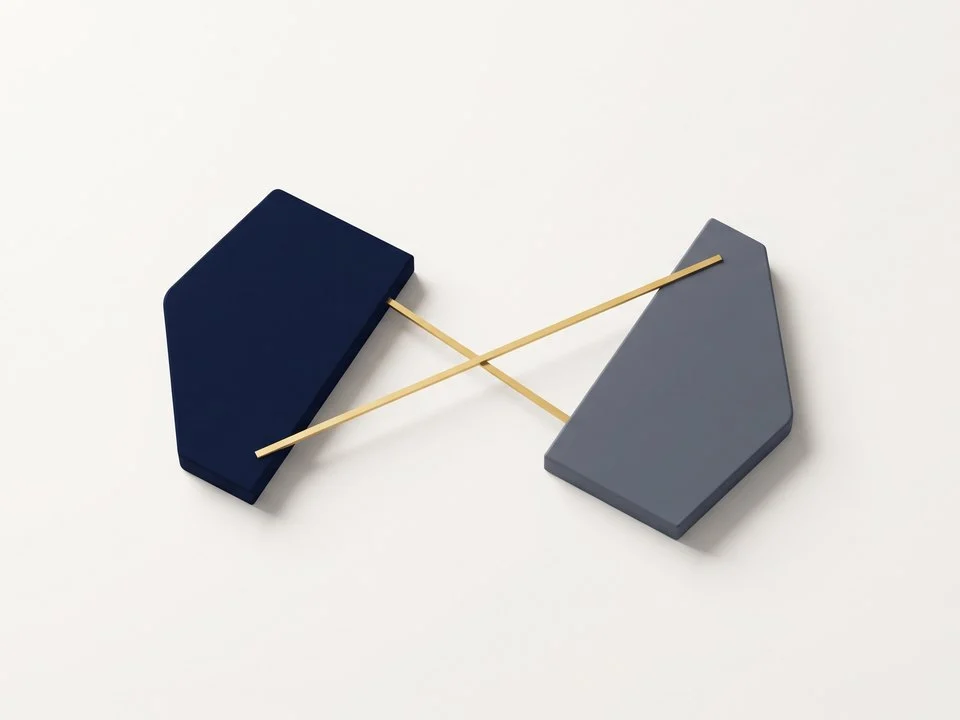 Composizione zenitale su superficie bianca calda con due blocchi geometrici ceramici distinti, uno blu marino e uno grigio, sormontati da una sottile linea metallica dorata orizzontale.
