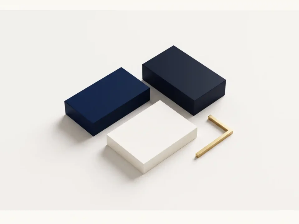 Composizione geometrica dall’alto su superficie bianca calda con tre blocchi rettangolari lisci nei toni del blu navy, blu scuro e bianco caldo, affiancati da un elemento angolare minimalista in ottone dorato opaco, senza scritte né loghi.